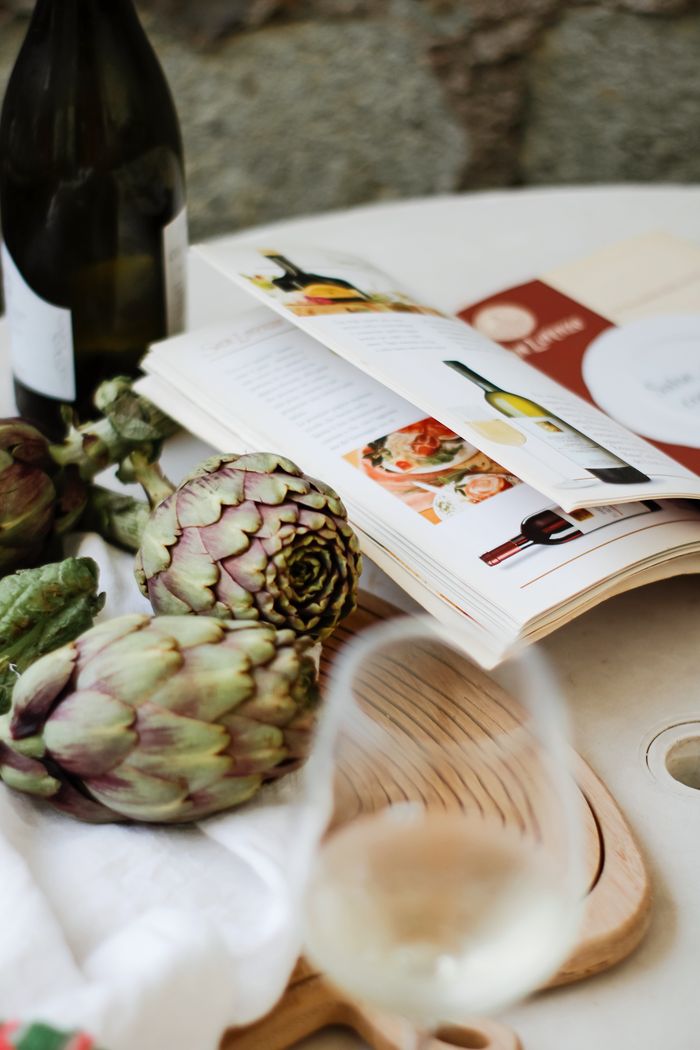 Elegant still life of artichokes, wine, and cookbook on a table, perfect for culinary inspiration.